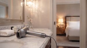 HD-818 Hair Dryer laying on its side on a bathroom counter with a faded shot of a luxurious hotel bedroom in the background