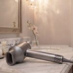 HD-818 Hair Dryer laying on its side on a bathroom counter with a faded shot of a luxurious hotel bedroom in the background